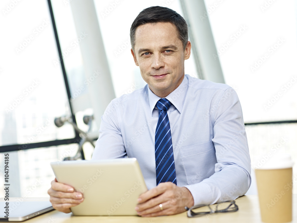 businessperson sitting in office holding ipad looking at camera