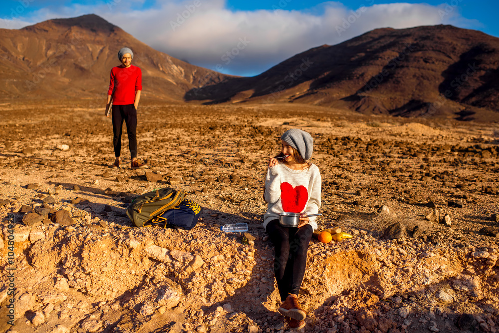 Young couple travelers working with laptop and having small picnic on the desert mountain landscape 