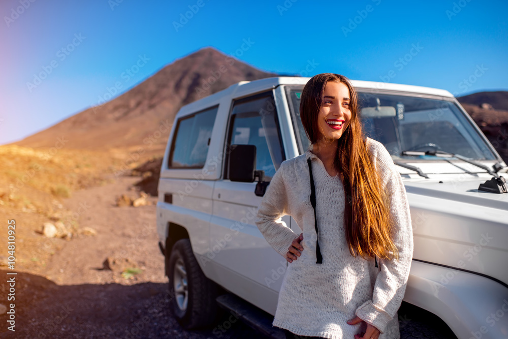 年轻漂亮的女人穿着毛衣，站在荒芜多石的土地上的白色吉普车附近