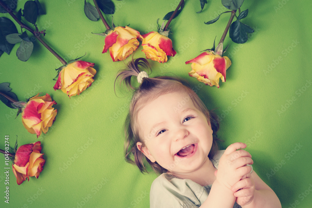 pretty little girl lying on green blanket with yellow roses