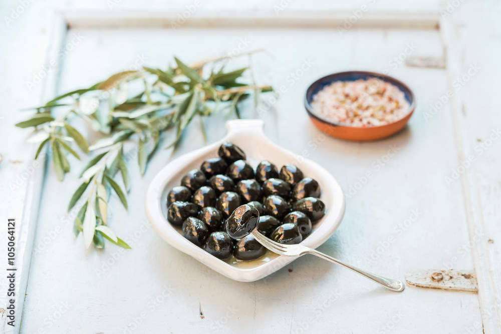 Black olives in white ceramic plate, branches and spices over li