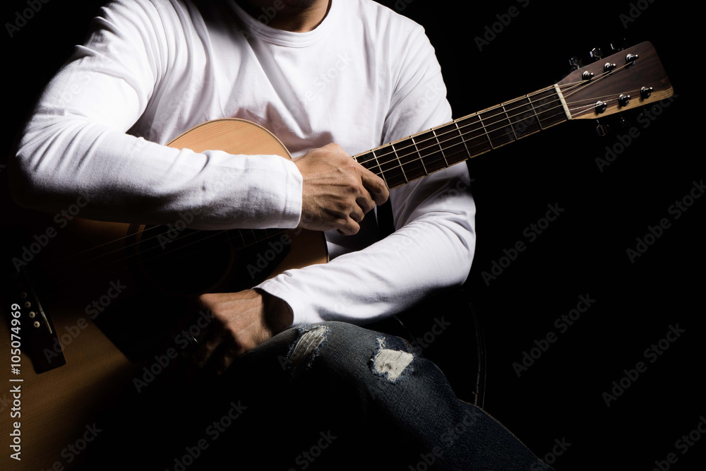 Asian man with white long sleeve shirt holding his guitar, dark low key lighting set up on black bac