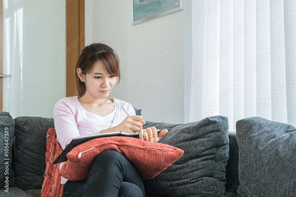 Asian young woman writing on couch at home in the living room