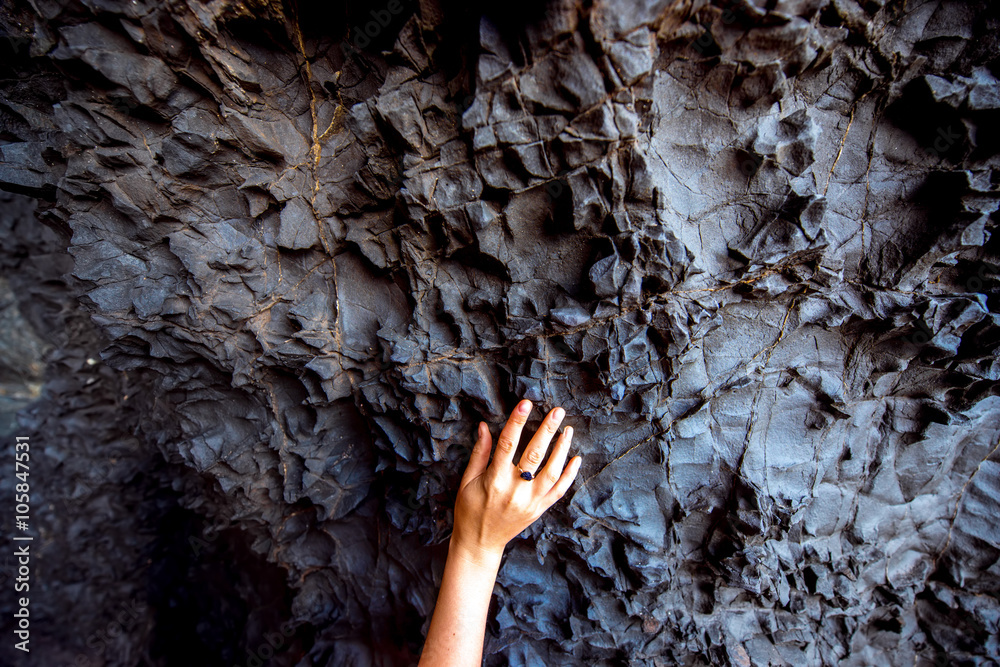 Close-up view on volcanic black rock with female hand in Ajiy caves on Fuerteventura island