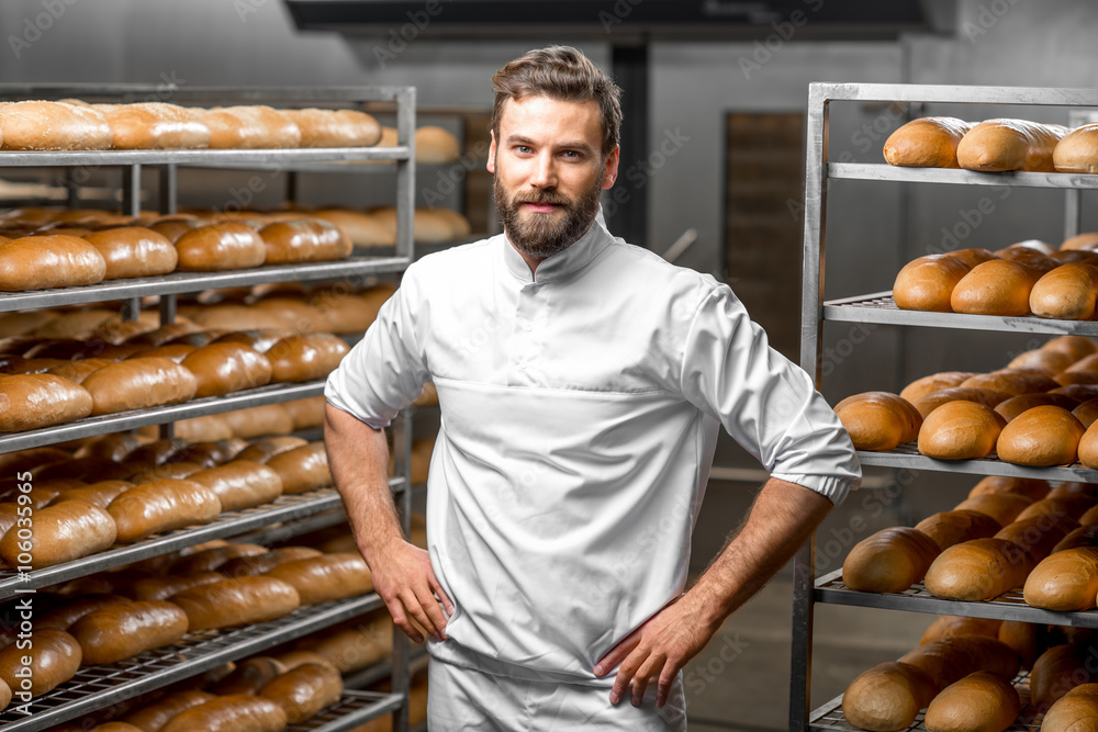 Portrait of handsome baker at the bakery with breads and oven on the background