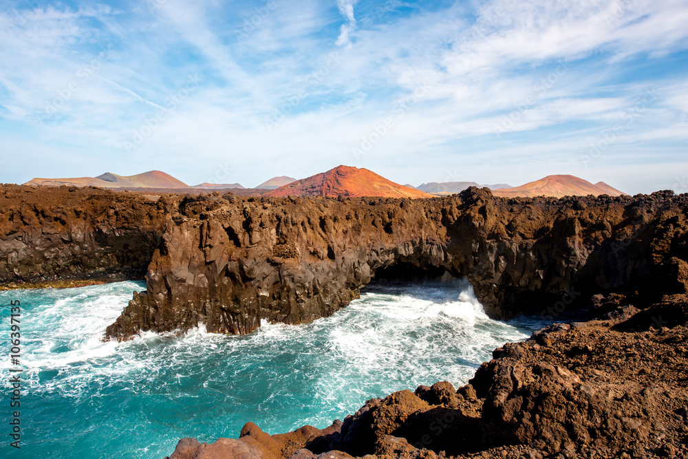 Los Hervideros rocky coast with wavy ocean and volcanos on the background on Lanzarote island in Spa