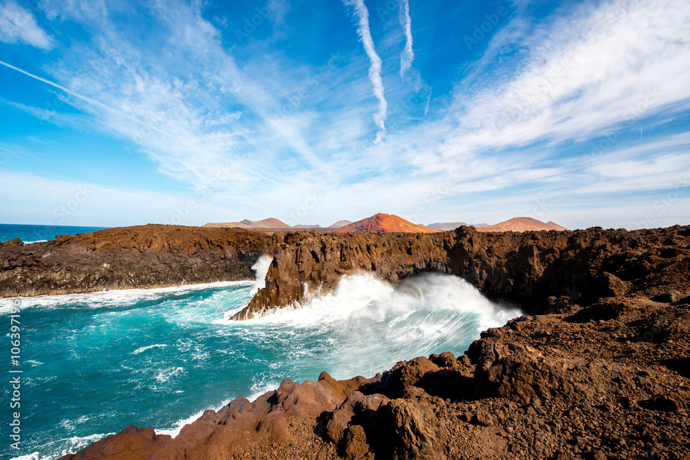 Los Hervideros rocky coast with wavy ocean and volcanos on the background on Lanzarote island in Spa