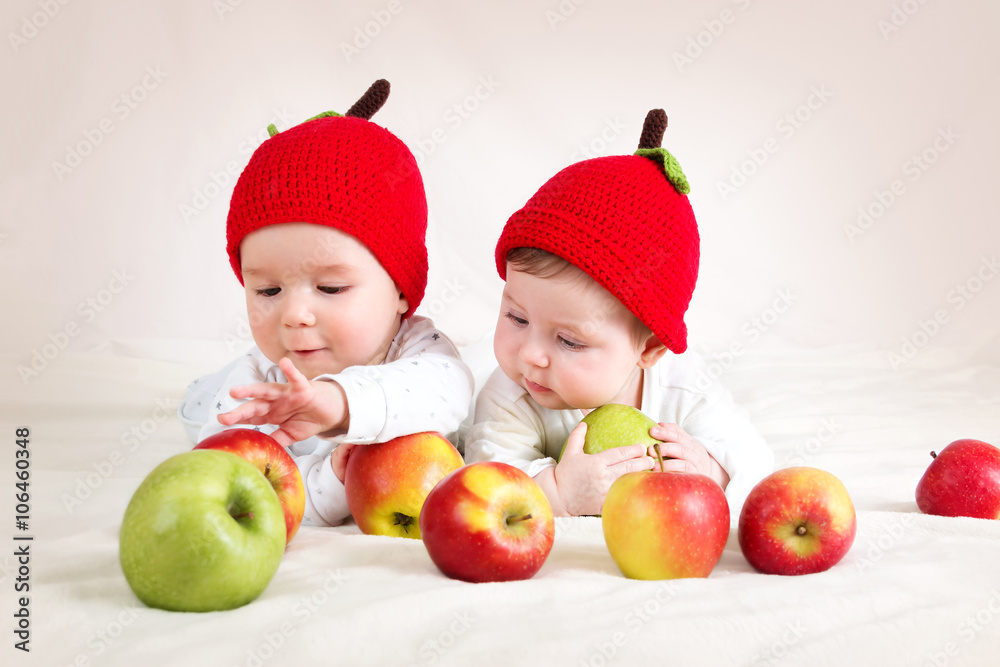 two cute babies lying in hats on soft blanket with apples