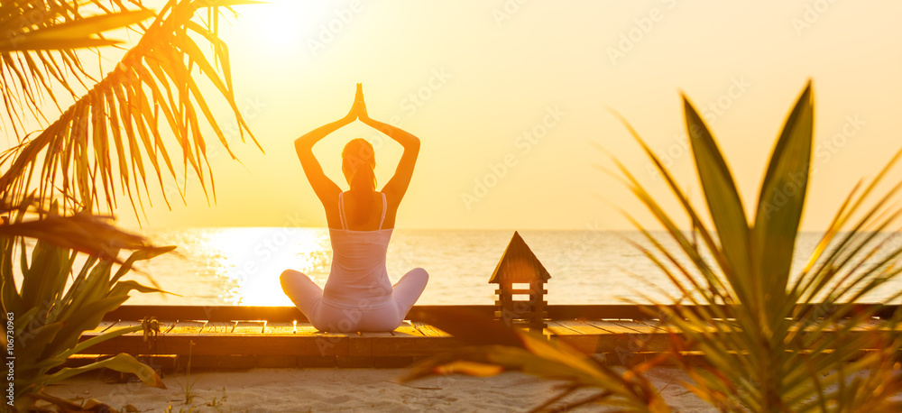 Young woman practicing yoga on the beach at sunset