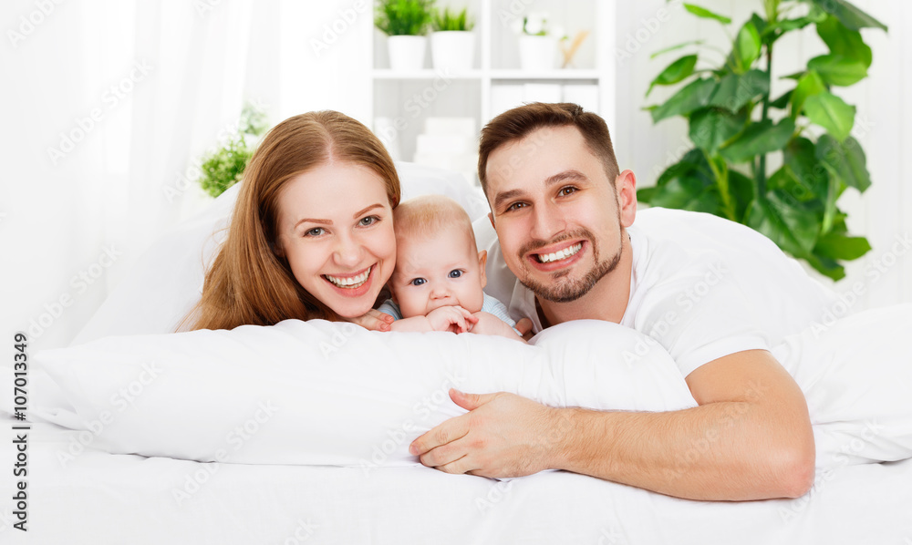 happy family of father, mother and baby playing in bed