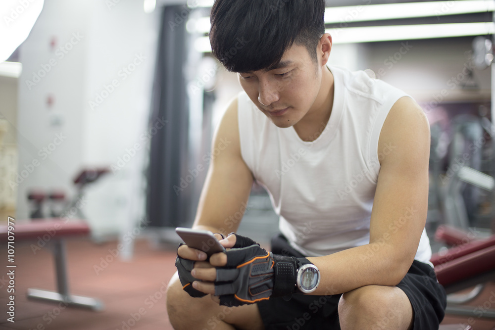 young handsome asian man using smart phone in modern gym