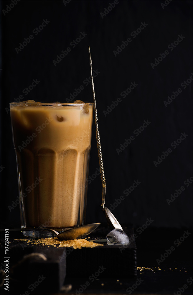 Iced coffee with milk in a tall glass, black background