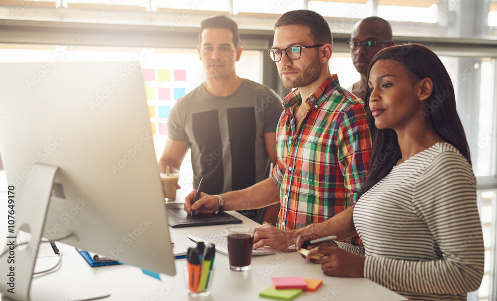 Four young workers standing around computer