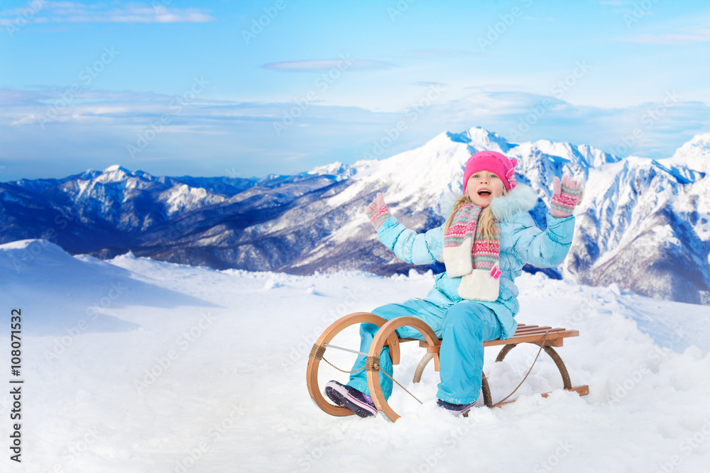 快乐的小女孩坐在山里的雪橇上