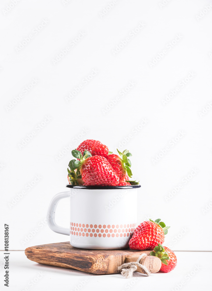 Fresh ripe red strawberries in country style enamel mug on rustic wooden board over white background