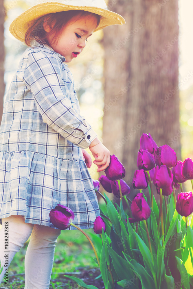 Toddler girl in a hat playing with tulips