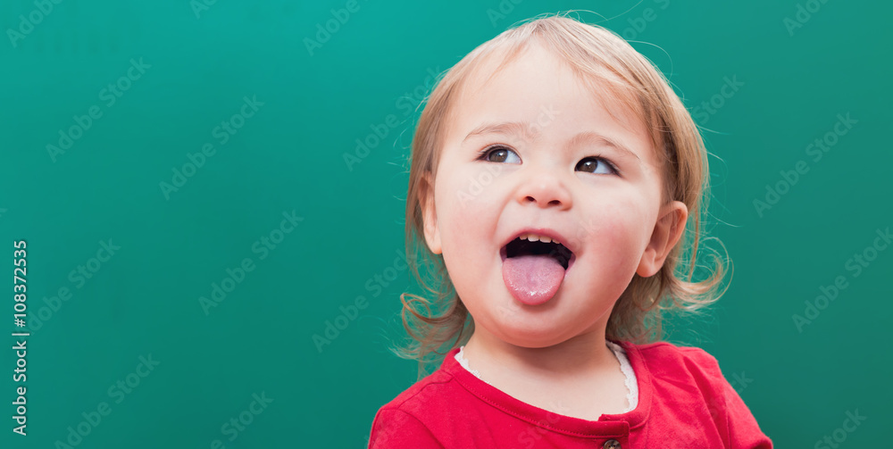 Happy toddler girl sticking her tongue out in front of a chalkboard