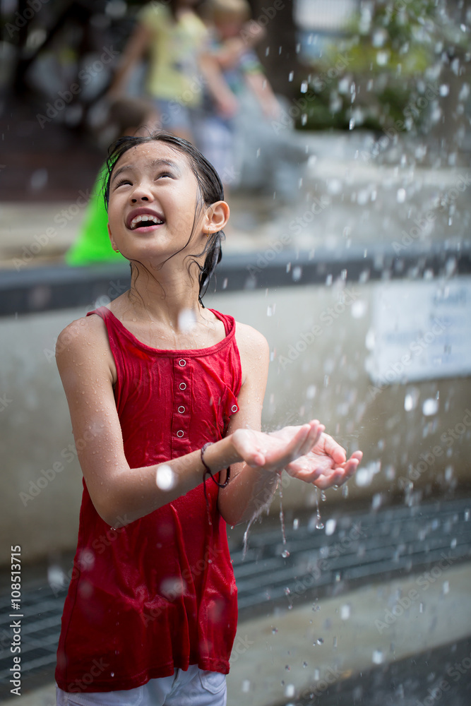 Asian girl playing with water fountain at water park