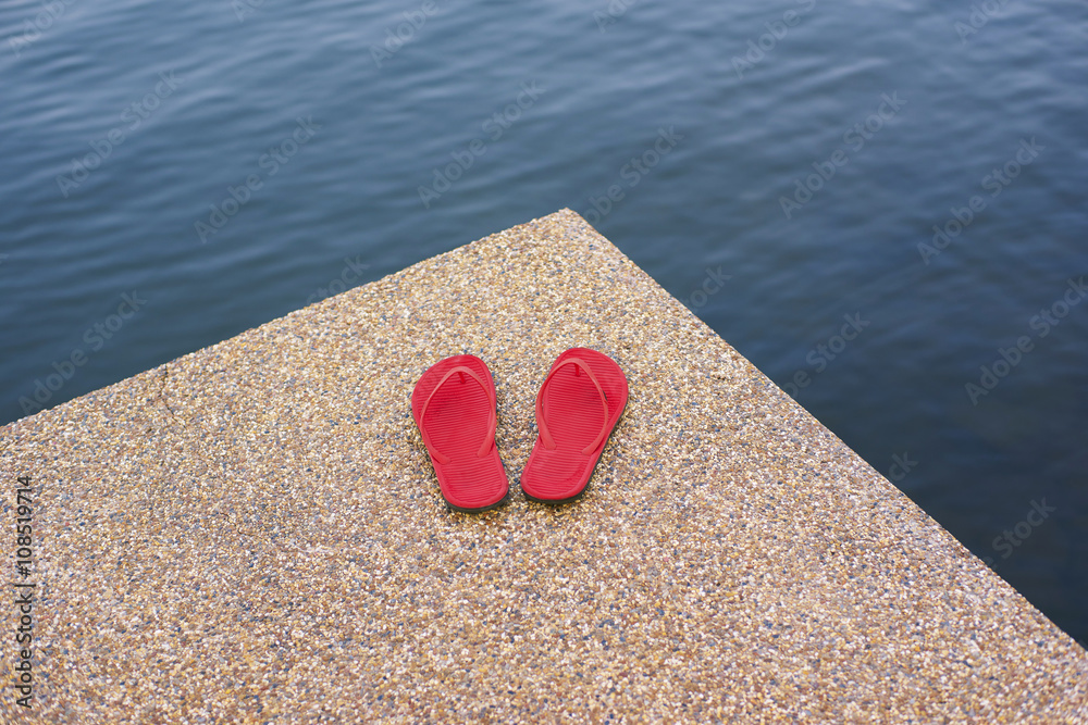 pair of red comfortable slipper placed lake side of stony floor