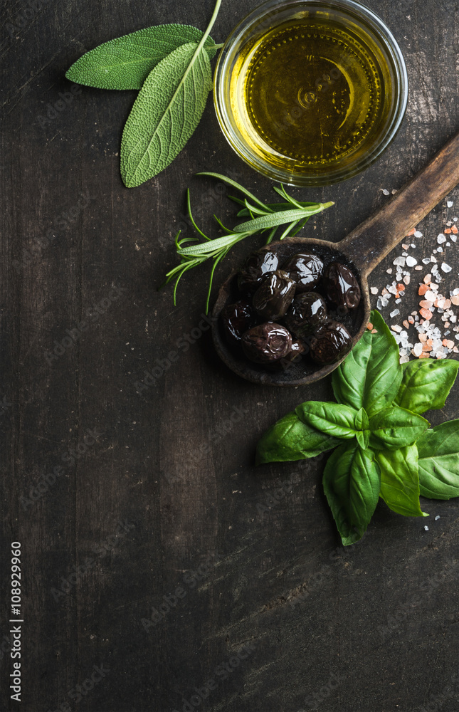 Greek black olives, fresh herbs and oil on dark rustic wooden background.