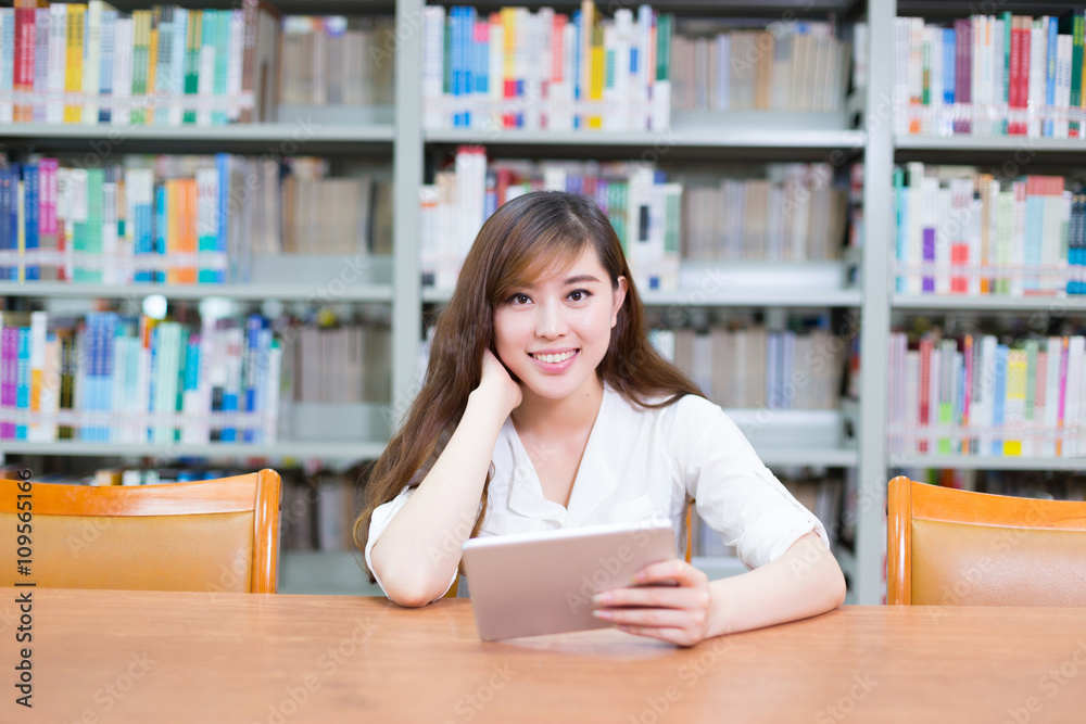 年轻漂亮的亚洲女孩在学校图书馆拿着平板电脑