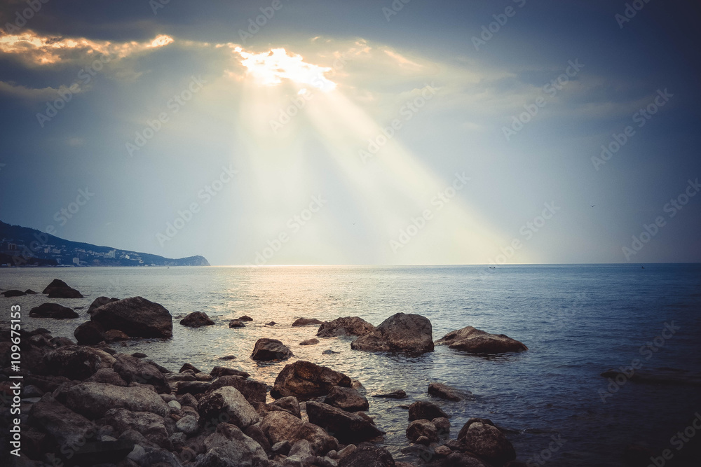 suns rays shine on the sea and rocky shore