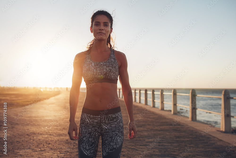 Confident sportswoman standing on a seaside road at evening