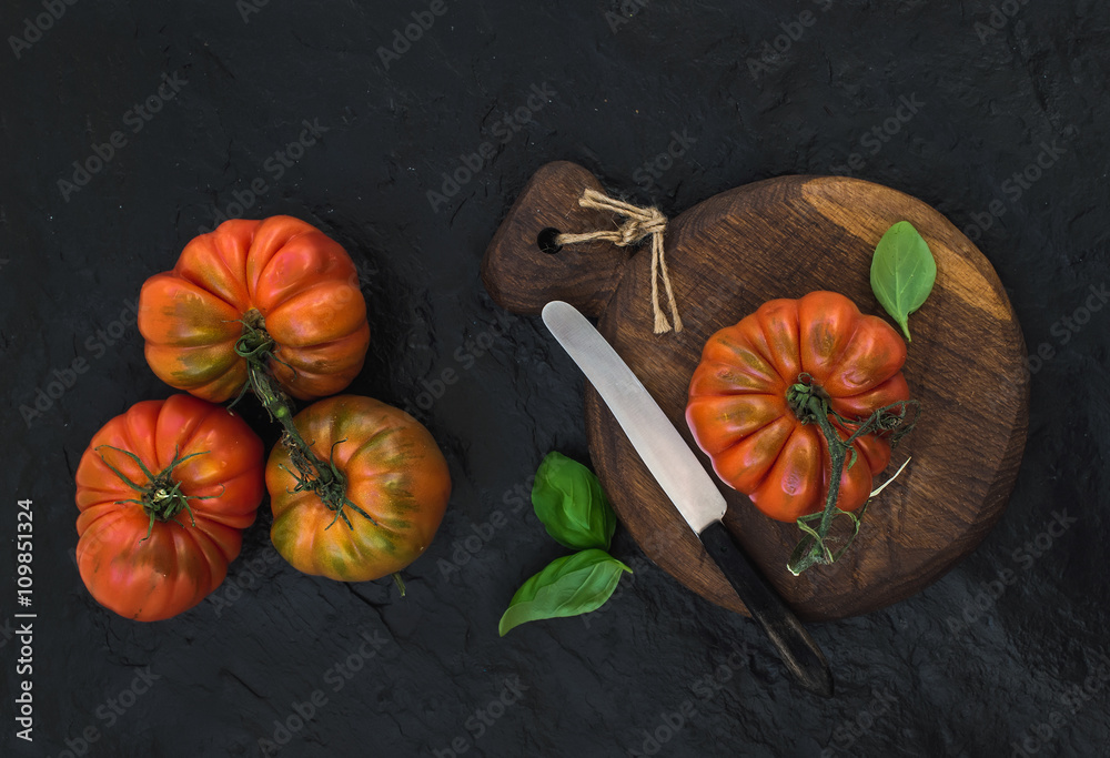 Fresh ripe hairloom tomatoes and basil leaves on rustic wooden board