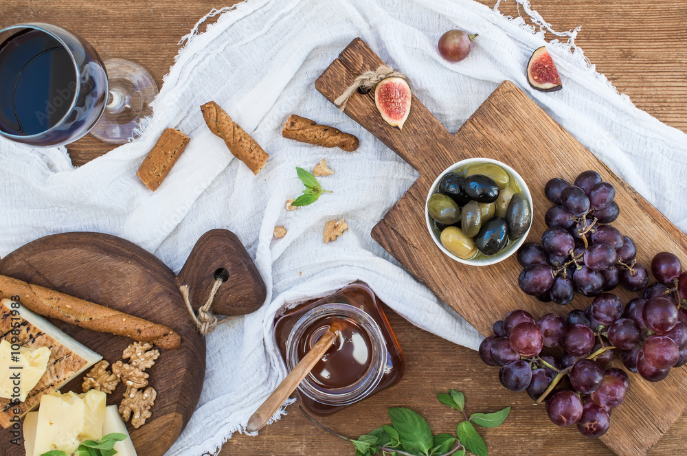 Glass of red wine, cheese board, grapes, walnuts, olives, honey and bread sticks