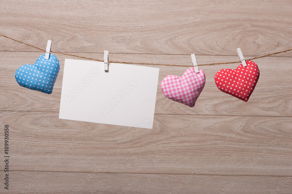 Blank instant photo and small red paper heart hanging on the clothesline. On white wooden background