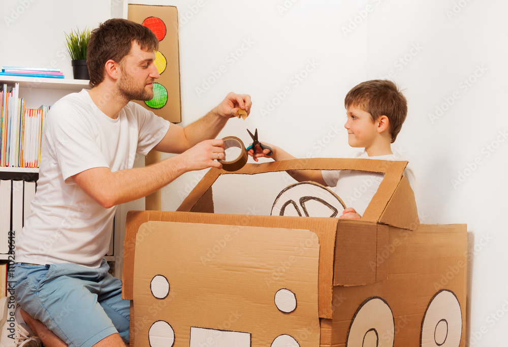 Dad and son making big toy cardboard car at home