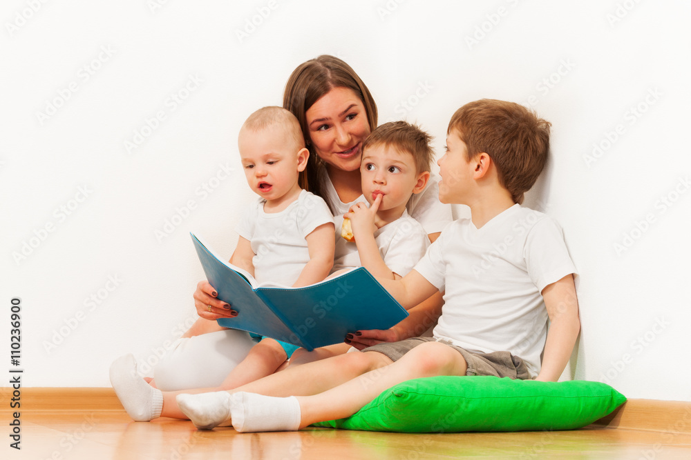 Young mother reading book to her age-diverse kids