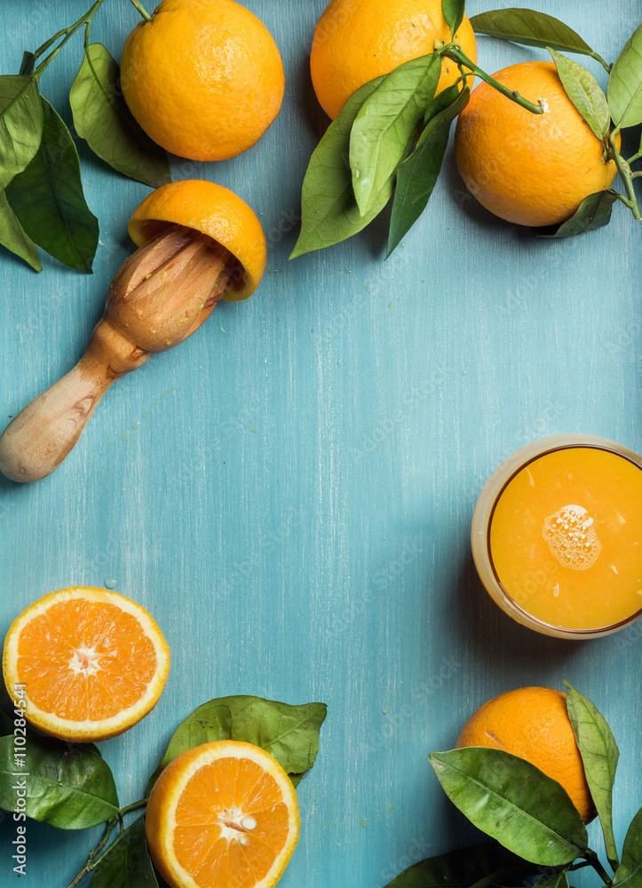 Fresh orange juice in glass and oranges with leaves on wooden turquoise blue painted background