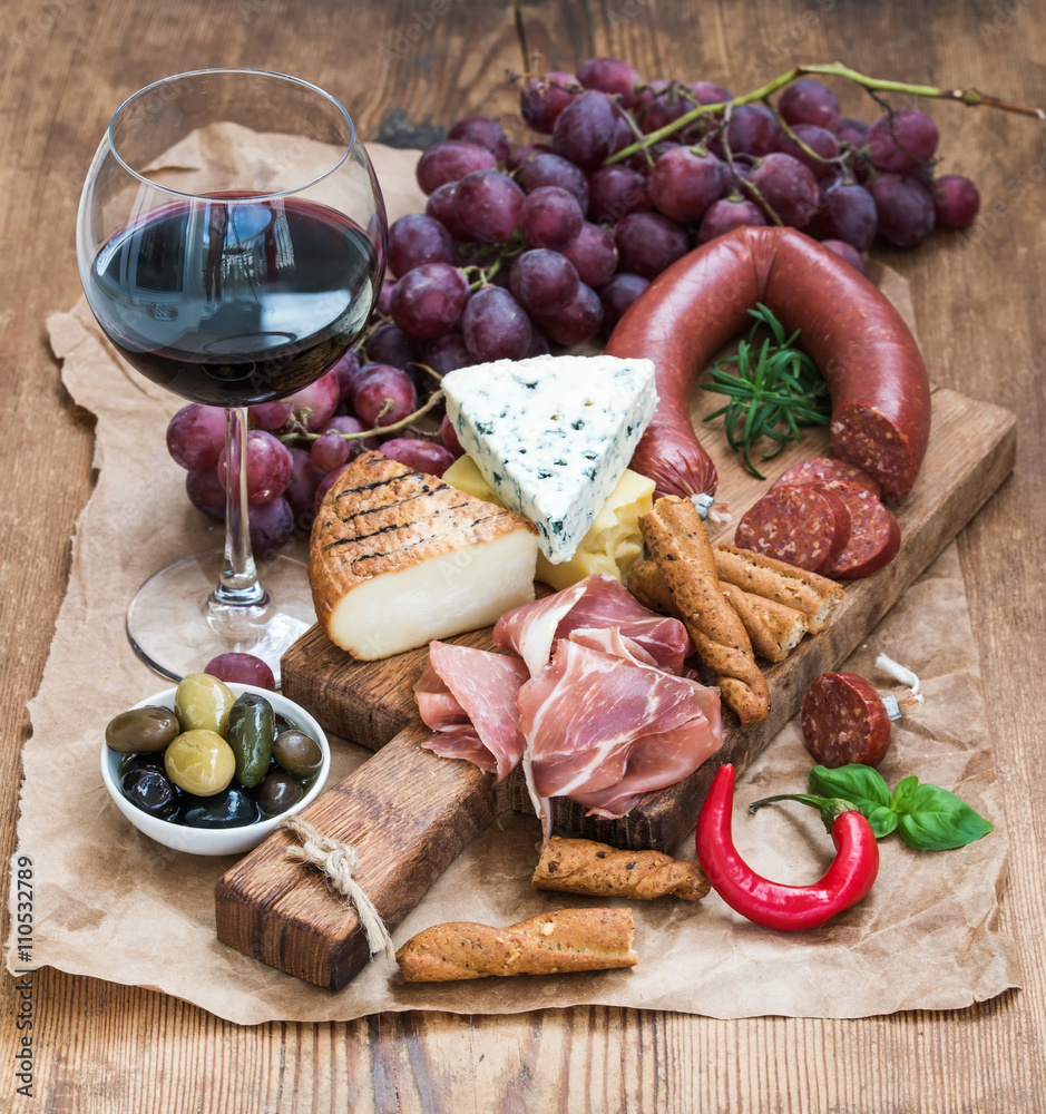 Glass of red wine, cheese and meat board, grapes,fig, strawberries, honey, bread sticks  on rustic w