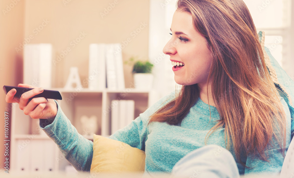 Young woman smiling while watching TV in her house