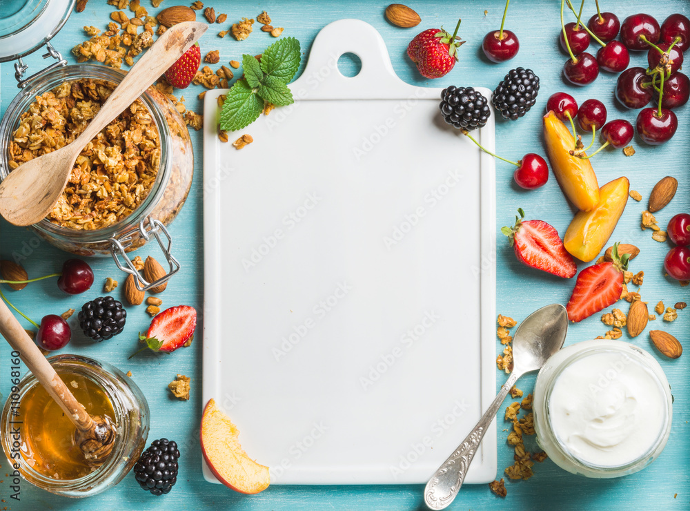 Healthy breakfast ingredients. Oat granola in open glass jar, yogurt, fruit, berries, honey and mint