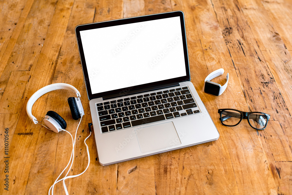 Laptop with white screen with earphones, smart watch, glasses on the wooden table