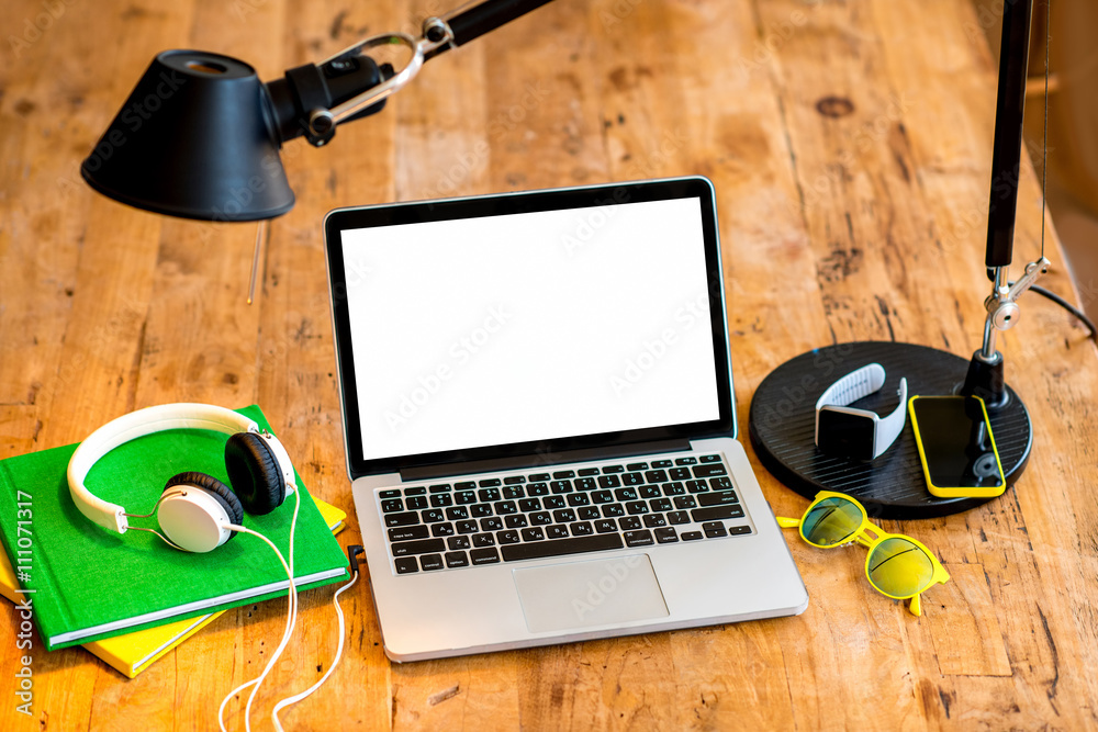 Laptop with white screen with earphones, smart watch, books, smart phone glasses and lamp on the woo