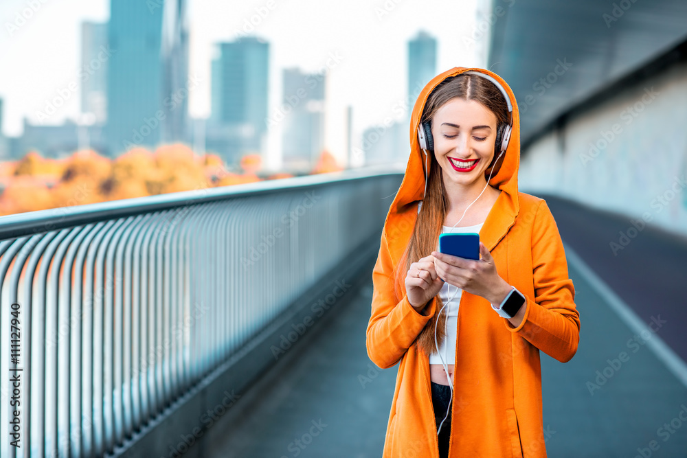 Young sport woman in yellow sweater listening to the music with smart phone on the modern bridge wit