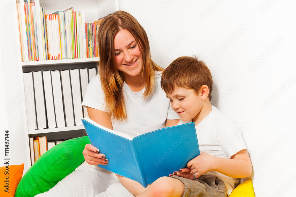 Smiling woman teaching her kid boy to read