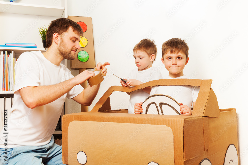 Father and his sons making toy car of cardboard