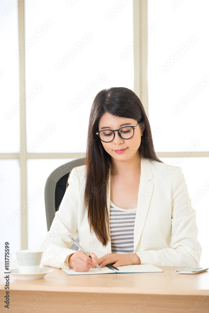 Young Asia businesswoman smiling and writing at desk