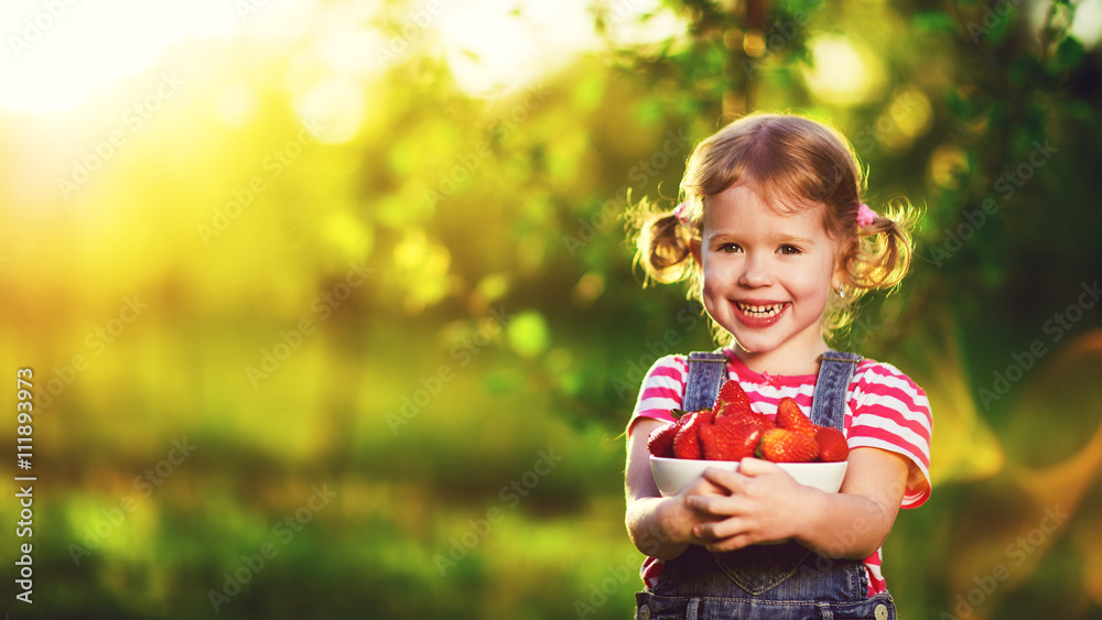 happy laughing child girl with ripe strawberry in summer on natu