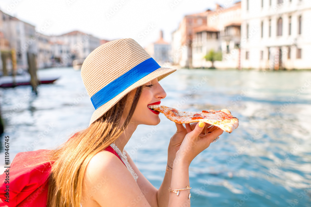 年轻的女性旅行者在威尼斯的运河背景下吃传统的意大利披萨片