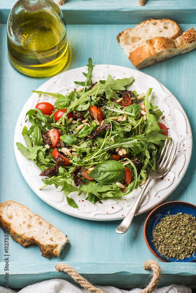 Salad with arugula, cherry tomatoes, pine nuts and herbs on white ceramic plate over blue wood backg