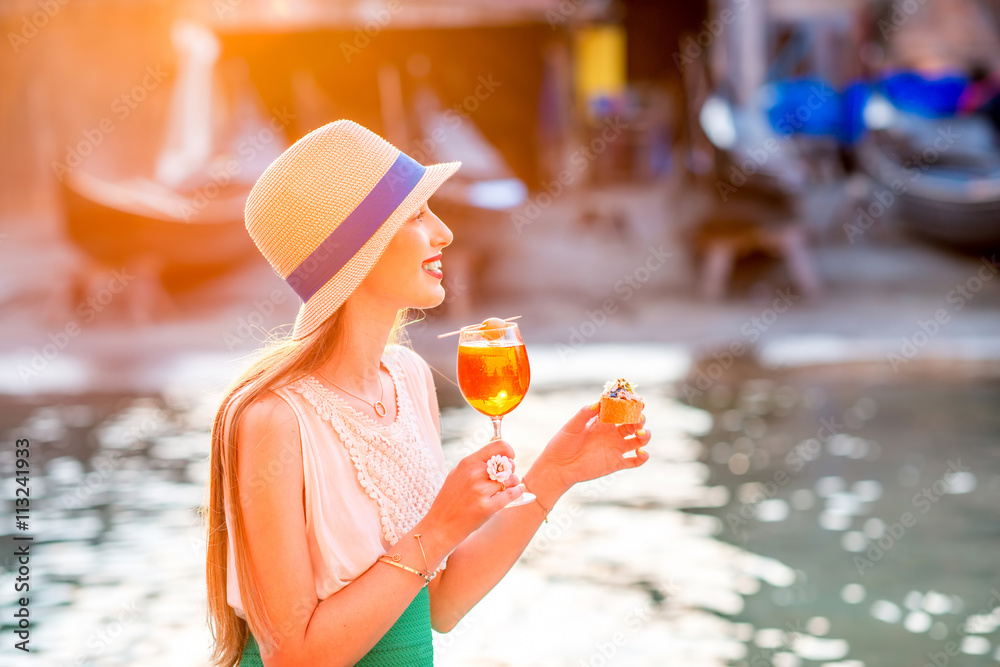 Young woman with glass of Spritz Aperol and italian snacks cicchetti sitting near the water chanal i