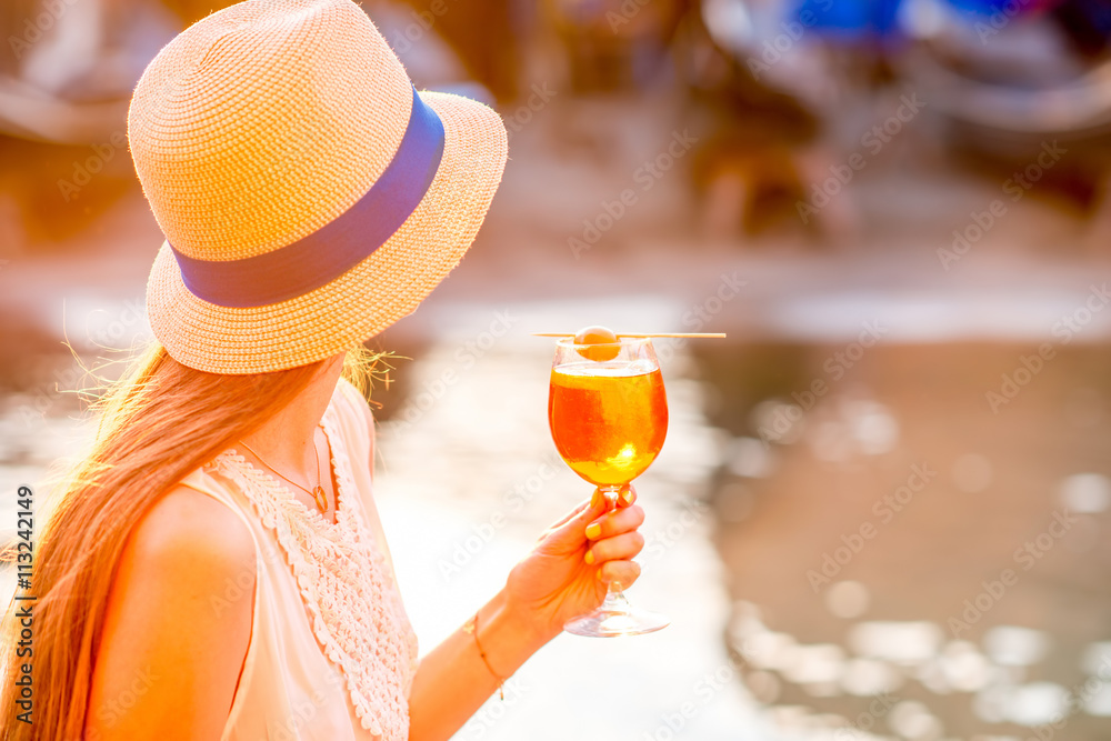 Young woman with glass of Spritz Aperol sitting near the water chanal in Venice on the sunset. Tradi