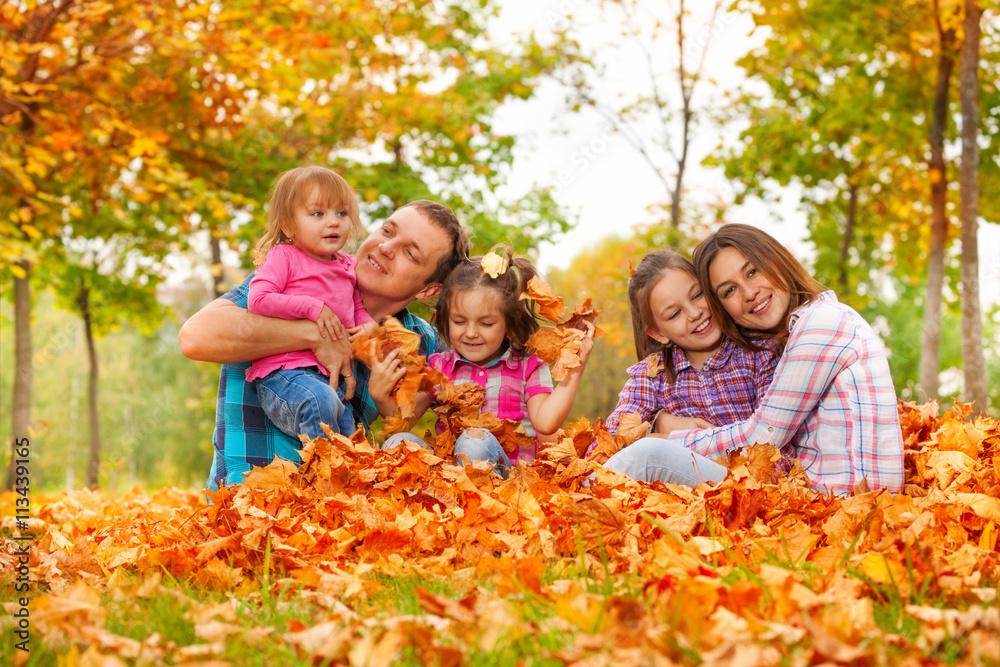 Mom, dad and daughters play in maple leaves pile