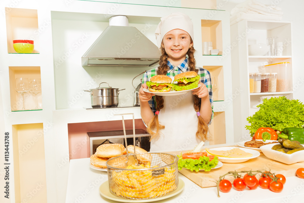 Cute girl holding plate with hamburgers at kitchen