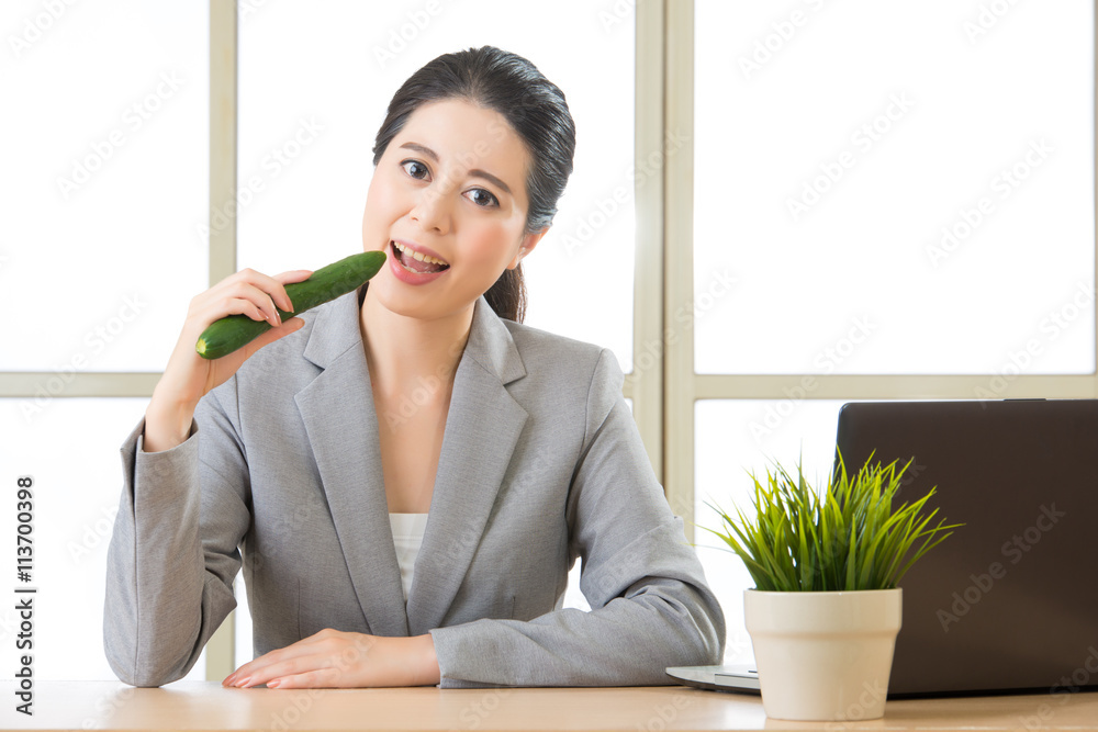 Young asian businesswoman eating healthy snack, cucumber